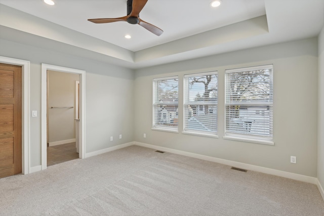 unfurnished bedroom featuring a walk in closet, light colored carpet, ceiling fan, and a tray ceiling