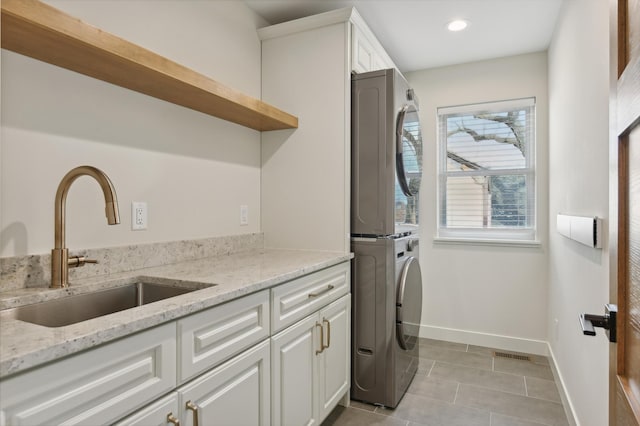 laundry room with stacked washer and dryer, light tile patterned flooring, cabinets, and sink