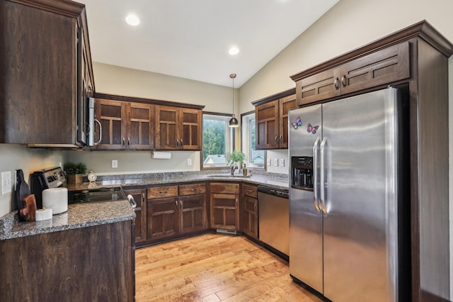 kitchen featuring appliances with stainless steel finishes, vaulted ceiling, sink, light hardwood / wood-style flooring, and dark stone countertops