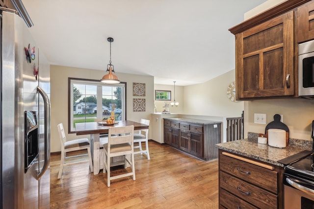 kitchen with appliances with stainless steel finishes, dark stone counters, decorative light fixtures, a notable chandelier, and light hardwood / wood-style floors