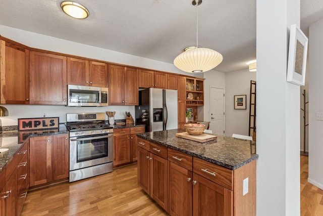 kitchen featuring appliances with stainless steel finishes, decorative light fixtures, dark stone counters, a textured ceiling, and light wood-type flooring