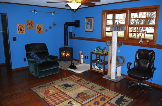 living area with hardwood / wood-style floors, a wood stove, ceiling fan, and crown molding