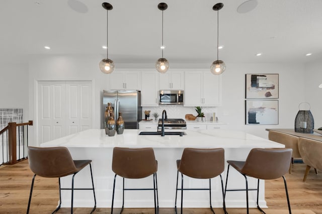 kitchen with decorative light fixtures, white cabinetry, a kitchen island with sink, and appliances with stainless steel finishes