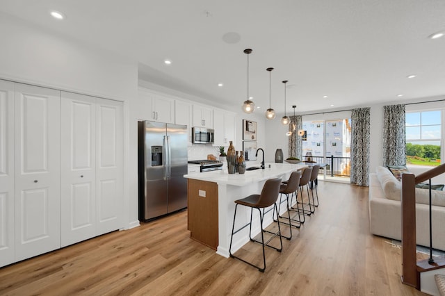 kitchen with stainless steel appliances, an island with sink, decorative light fixtures, a breakfast bar, and white cabinets