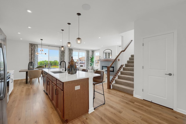 kitchen with pendant lighting, light hardwood / wood-style floors, sink, and an island with sink