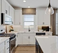 kitchen with a healthy amount of sunlight, white cabinets, sink, hanging light fixtures, and gas stove