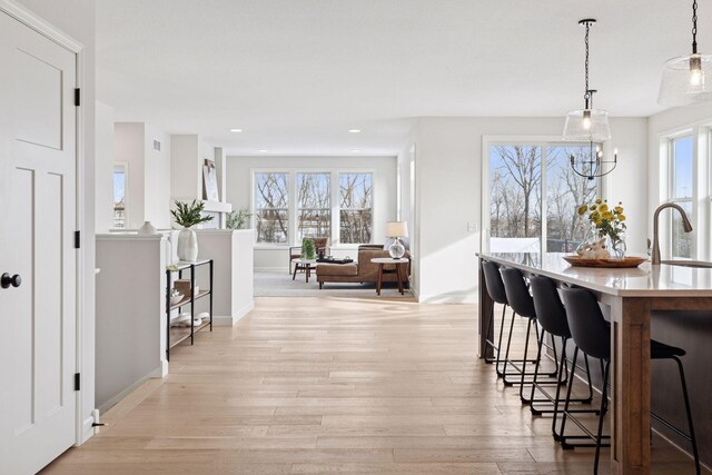 hall featuring light wood finished floors, recessed lighting, baseboards, and a sink