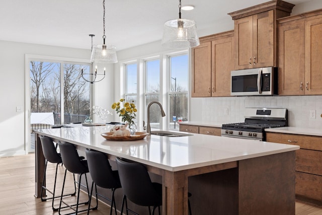 kitchen featuring backsplash, a center island with sink, light countertops, stainless steel appliances, and a sink