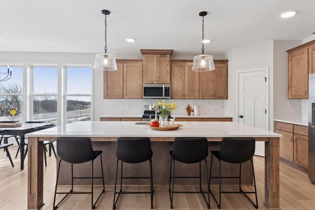 kitchen with light countertops, decorative backsplash, light wood-style flooring, appliances with stainless steel finishes, and a kitchen island with sink