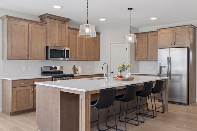 kitchen with light wood-type flooring, stainless steel appliances, an island with sink, and a sink