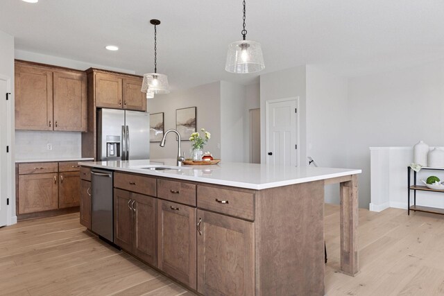 kitchen featuring light wood-type flooring, a sink, stainless steel appliances, light countertops, and hanging light fixtures