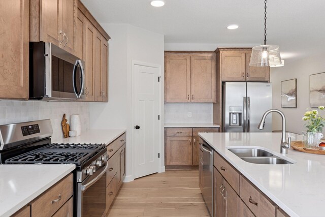 kitchen featuring a sink, stainless steel appliances, light countertops, light wood-style floors, and brown cabinets