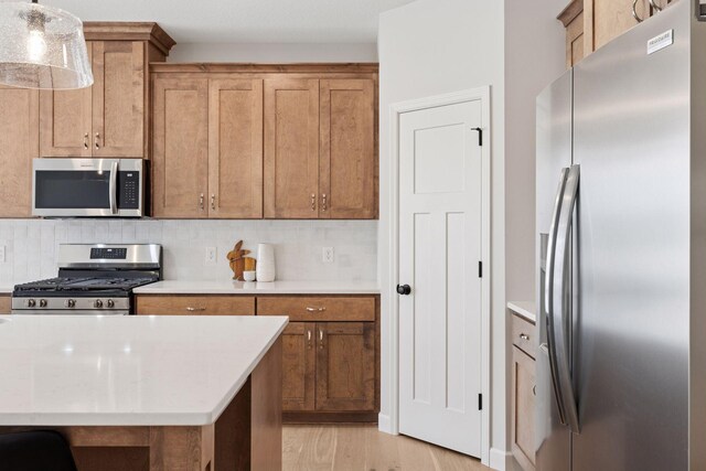 kitchen with stainless steel appliances, light wood-style flooring, decorative backsplash, and light countertops