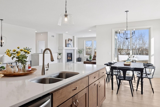 kitchen featuring a glass covered fireplace, stainless steel dishwasher, a chandelier, and a sink