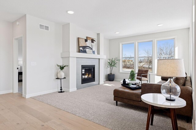 living area with wood finished floors, visible vents, baseboards, and a glass covered fireplace