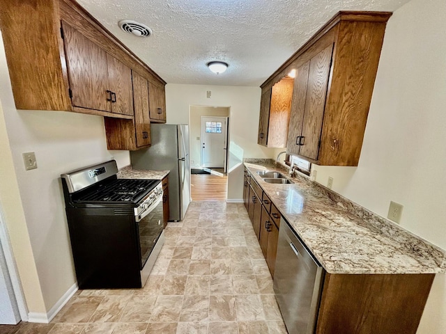 kitchen featuring appliances with stainless steel finishes, sink, a textured ceiling, and light stone counters