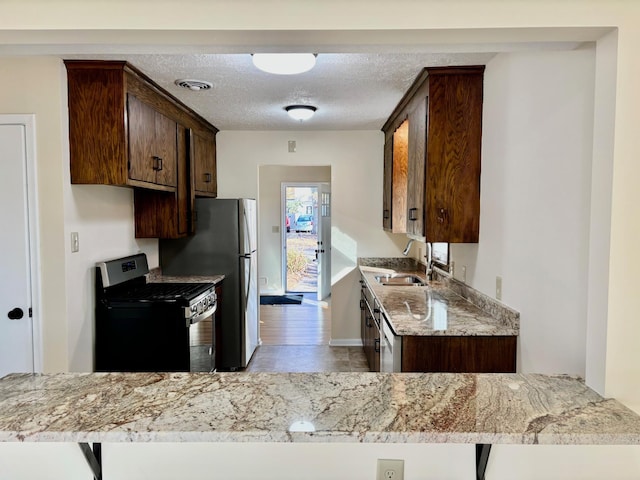 kitchen with light stone countertops, appliances with stainless steel finishes, kitchen peninsula, and a textured ceiling