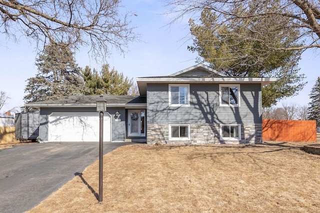 split level home featuring a garage, aphalt driveway, and fence