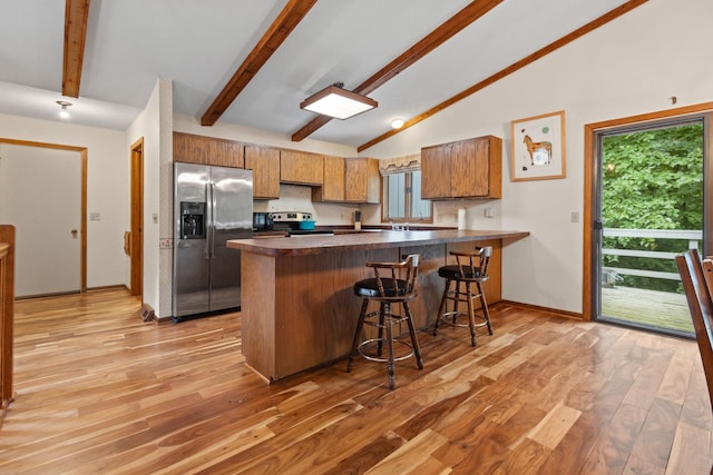 kitchen with stainless steel appliances, lofted ceiling with beams, kitchen peninsula, light hardwood / wood-style floors, and a kitchen bar