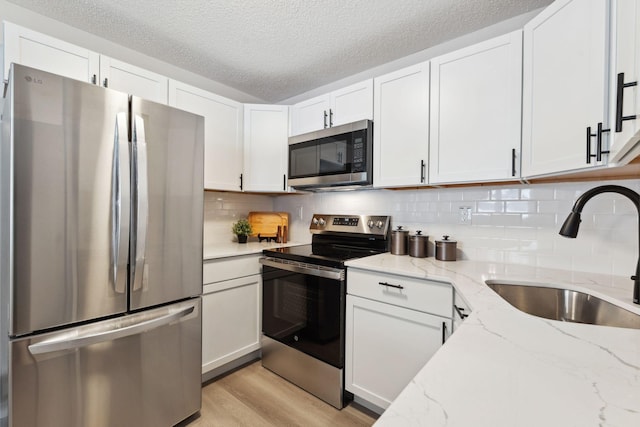 kitchen featuring sink, white cabinetry, appliances with stainless steel finishes, a textured ceiling, and light stone counters