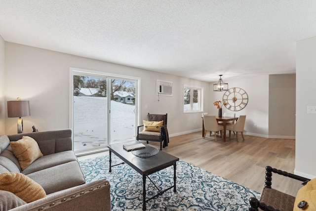 living room featuring an AC wall unit, an inviting chandelier, a textured ceiling, and light hardwood / wood-style flooring