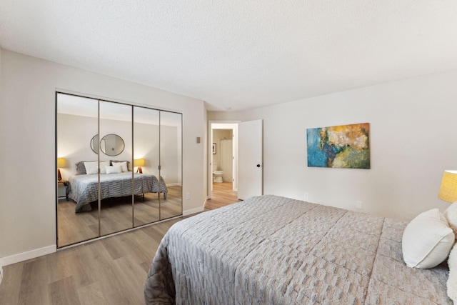 bedroom with ensuite bath, light wood-type flooring, a closet, and a textured ceiling