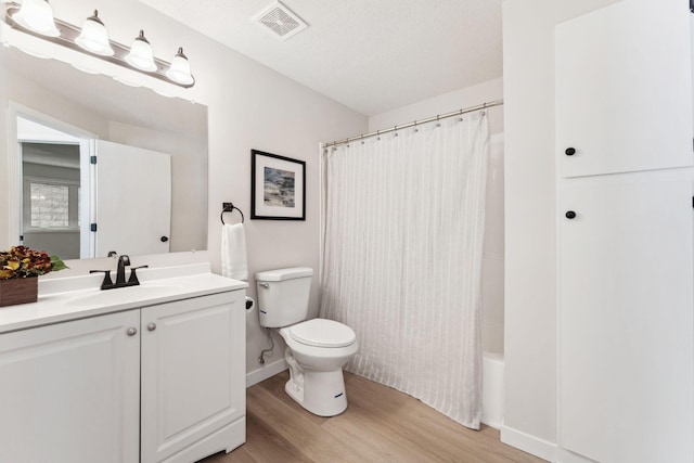 full bathroom with a textured ceiling, wood-type flooring, vanity, shower / tub combo, and toilet