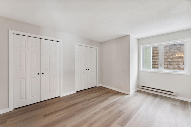 unfurnished bedroom featuring a baseboard radiator, a textured ceiling, two closets, and light wood-type flooring