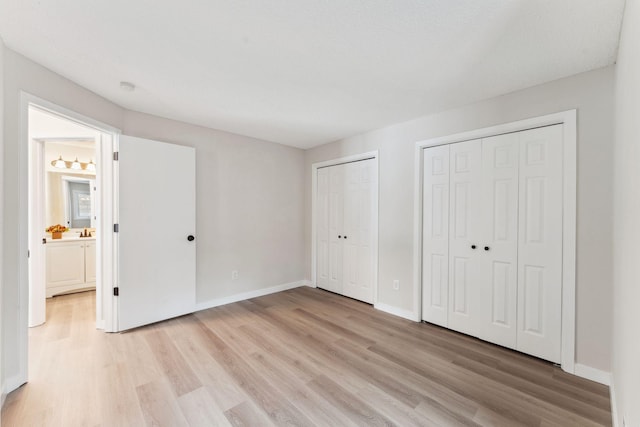 unfurnished bedroom with light hardwood / wood-style floors, ensuite bath, and multiple closets