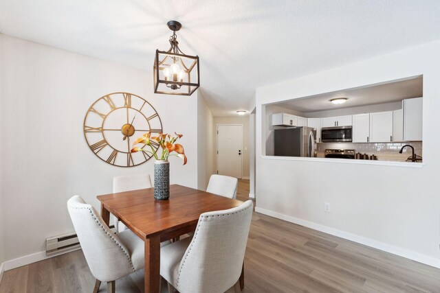 dining area featuring light wood-style floors, a baseboard heating unit, and baseboards