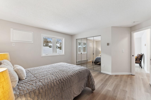 bedroom featuring a baseboard radiator, light wood-style flooring, baseboards, and a textured ceiling