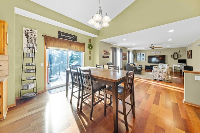 dining space with ceiling fan with notable chandelier, light hardwood / wood-style floors, and vaulted ceiling