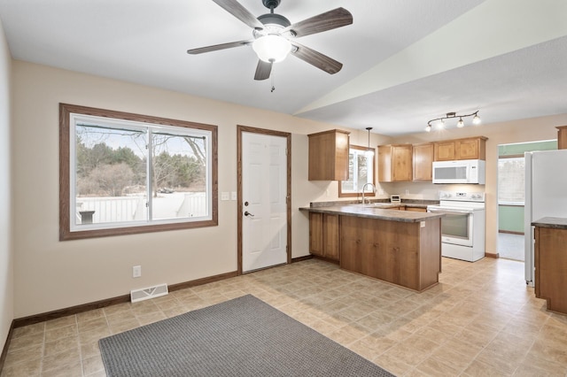 kitchen with a wealth of natural light, kitchen peninsula, lofted ceiling, decorative light fixtures, and white appliances