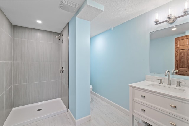 bathroom with a tile shower, vanity, a textured ceiling, hardwood / wood-style floors, and toilet