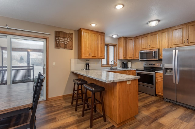 kitchen with a kitchen bar, stainless steel appliances, sink, dark hardwood / wood-style floors, and kitchen peninsula