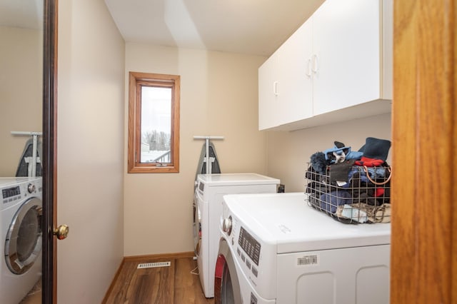 laundry room featuring wood-type flooring, separate washer and dryer, and cabinets