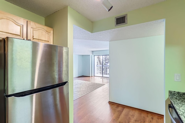 kitchen with light brown cabinets, a textured ceiling, stainless steel refrigerator, and light wood-type flooring