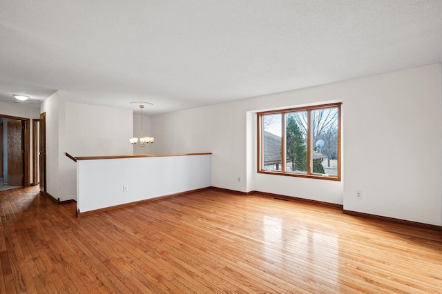 empty room featuring light wood-type flooring, a textured ceiling, and a notable chandelier