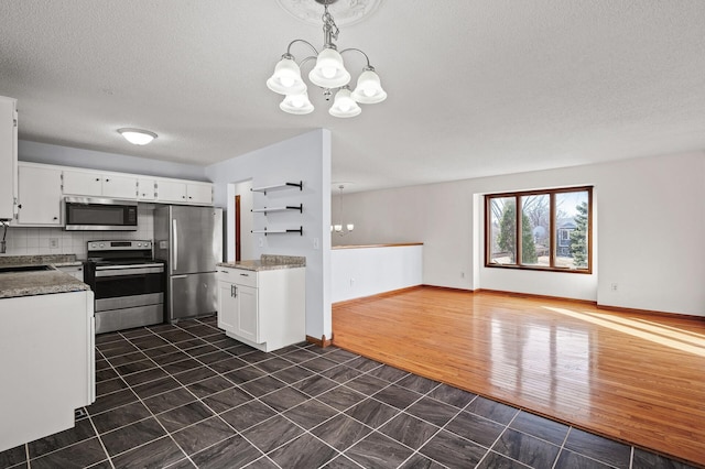 kitchen with white cabinetry, decorative light fixtures, a notable chandelier, stainless steel appliances, and backsplash