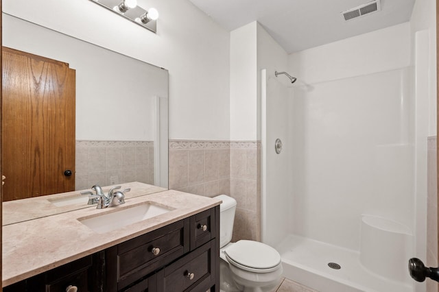 bathroom with tile walls, vanity, a shower, and toilet