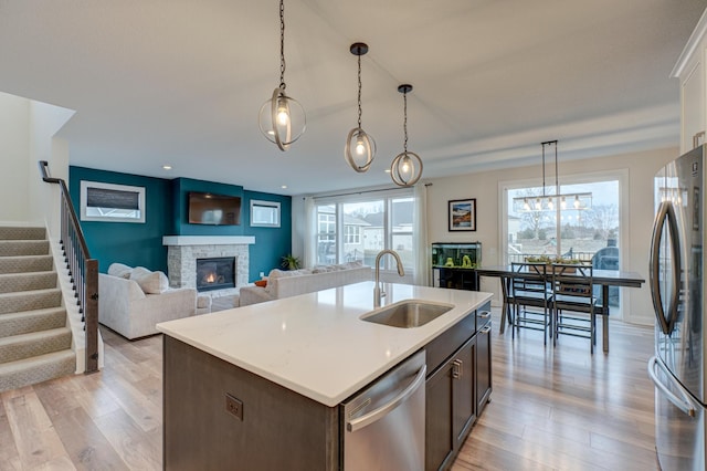 kitchen with sink, dark brown cabinets, a fireplace, a center island with sink, and appliances with stainless steel finishes