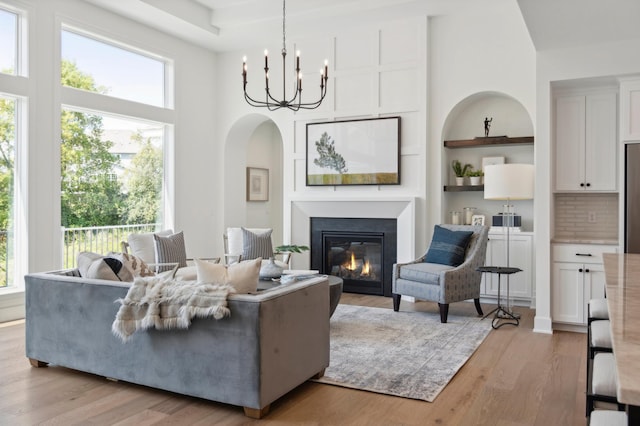 living room featuring built in features, light hardwood / wood-style flooring, a high ceiling, and a chandelier