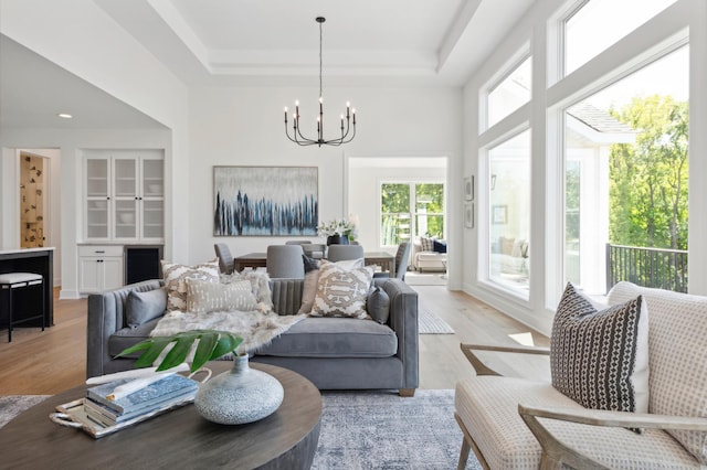 living room featuring a tray ceiling, a chandelier, and light wood-type flooring