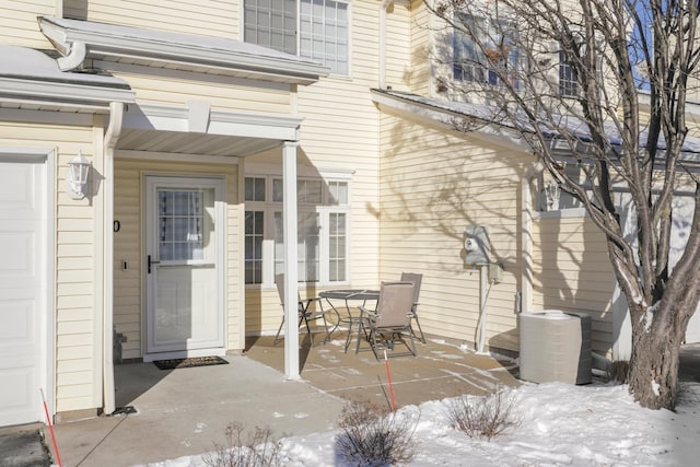 snow covered property entrance featuring a garage and central AC