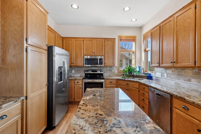 kitchen featuring light stone countertops, a sink, stainless steel appliances, light wood-style floors, and backsplash