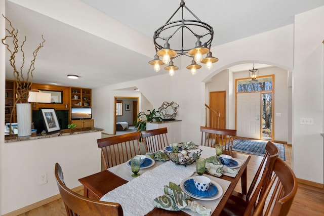 dining room featuring baseboards, arched walkways, light wood-style floors, and an inviting chandelier