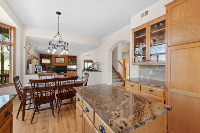 kitchen with light wood finished floors, visible vents, tasteful backsplash, glass insert cabinets, and open floor plan