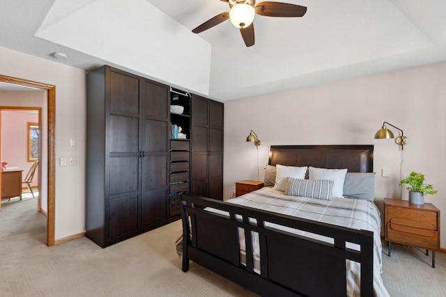 bedroom featuring light colored carpet, baseboards, a tray ceiling, and ceiling fan