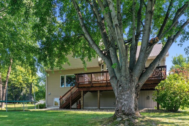 back of property featuring a deck, stairway, a trampoline, and a lawn