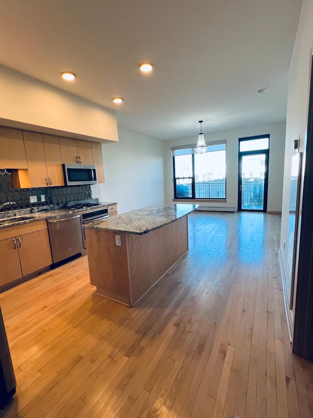 kitchen with stainless steel appliances, backsplash, dark stone counters, light hardwood / wood-style floors, and a kitchen island